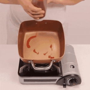 Verter salsa de tomate en una sartén 3 EN 1 COPPER CHEF calentada en una estufa portátil, demostrando la superficie antiadherente.