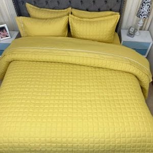 Edredón Tipo Quilt un solo tono acolchado amarillo ambientado en un dormitorio.