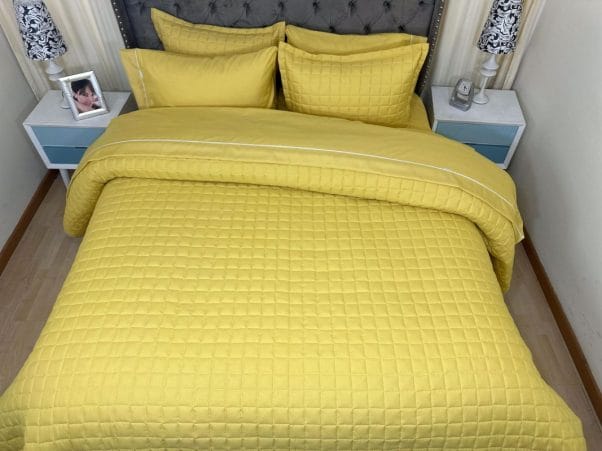 Edredón Tipo Quilt un solo tono acolchado amarillo ambientado en un dormitorio.
