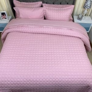 Una cama con Edredón Tipo Quilt un solo tono rosa y almohadas.